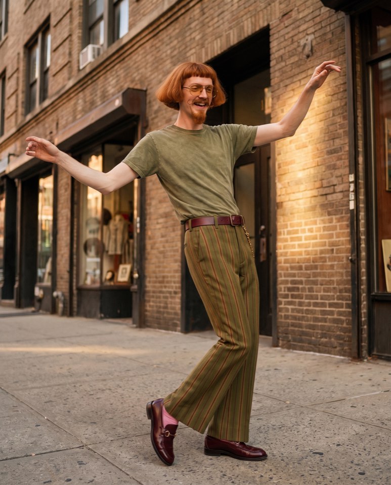 Tony dancing on a city sidewalk in an olive tee